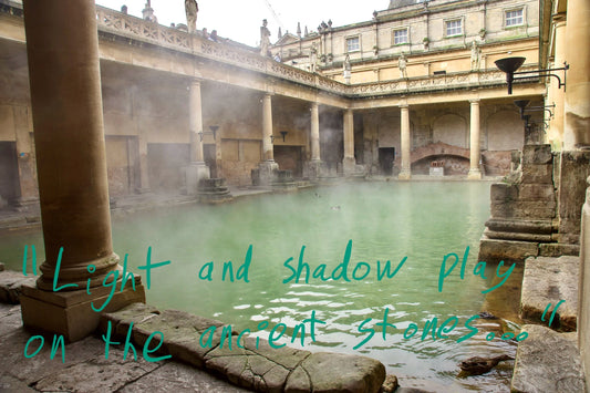 The Great Bath at the Roman Bath in Bath. Steam is emanating from the warm spring water, which has green hue. Graffiti overlay featuring a quote from the article: "Light and shadow play on the ancient stones"