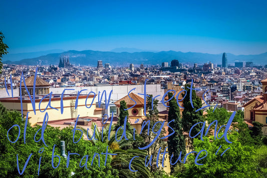 View over the sunlit Barcelona skyline, with La Sagrada Familia and the Glòries Tower poking out above the characteristically European flat cityscape. Graffiti overlay featuring a quote from the article: "Narrow streets, old buildings and vibrant culture"
