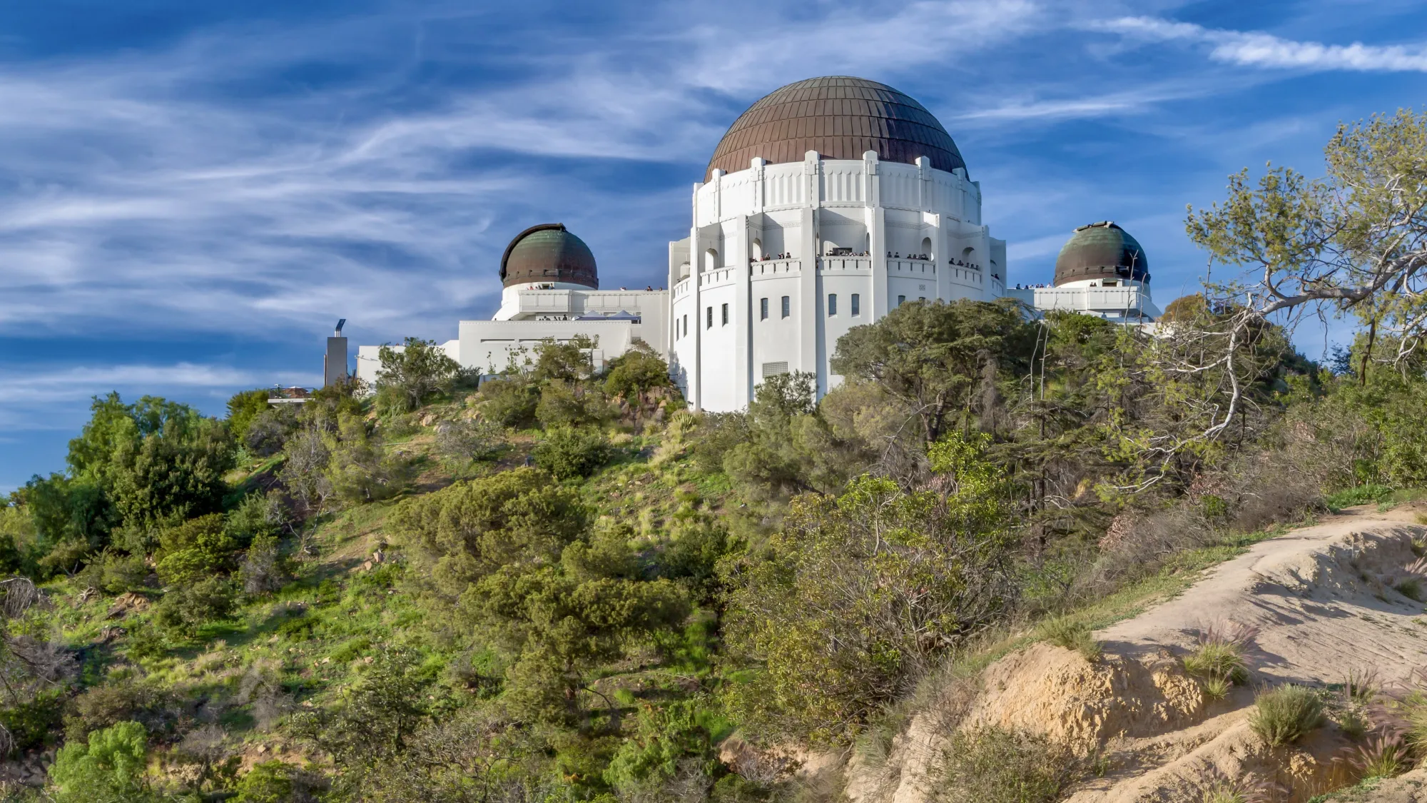 Looking up at Los Angeles' Griffith Observatory. Green vegetation in the foreground and a blue sky with wispy clouds in the background