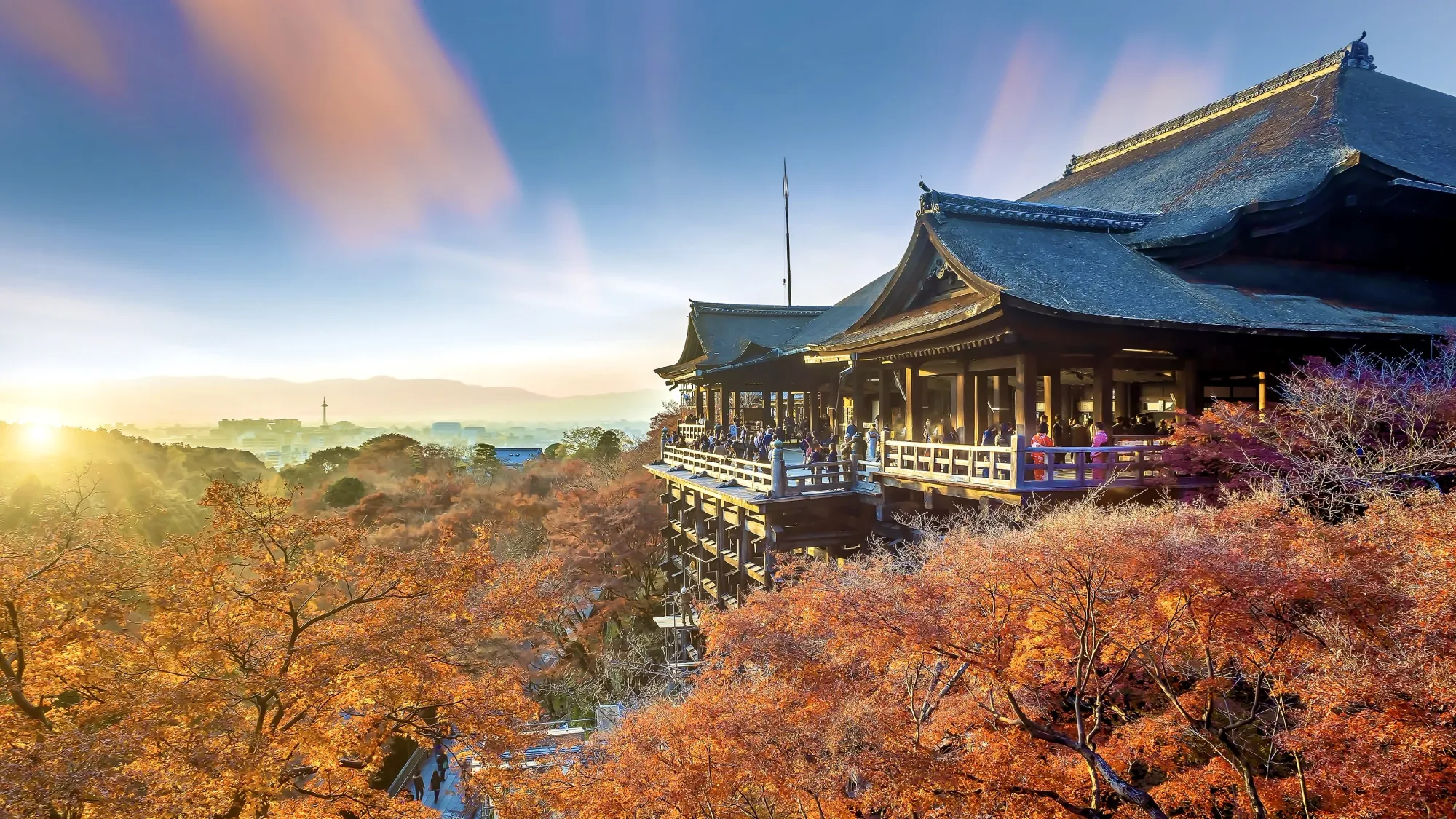 Kiyomizu-dera temple in Kyoto, Japan. The temple is surrounded by trees, covered in Autumnal foliage. The City of Kyoto can be seen in the distance.