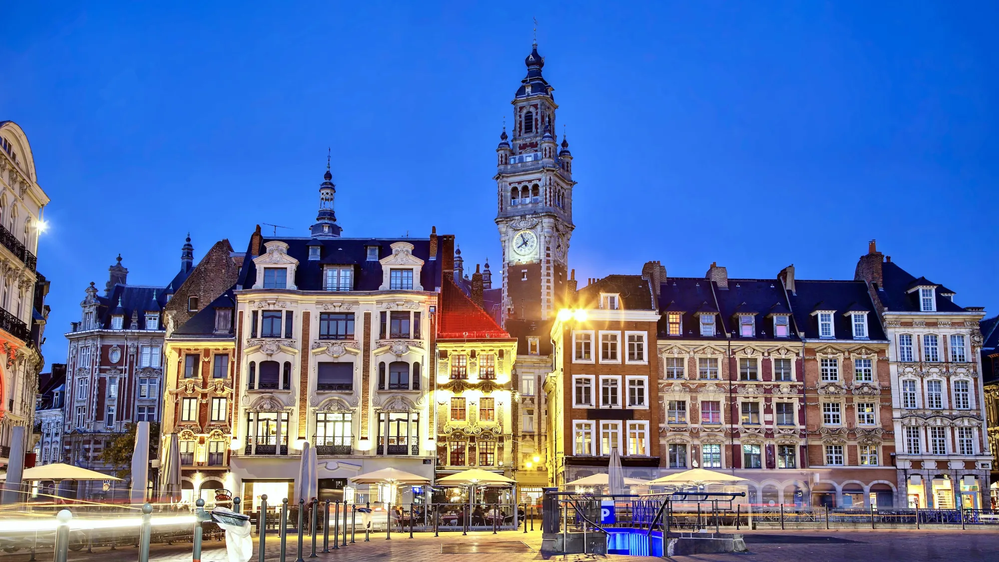 The Grand Place buildings in Lille at Dusk, the lights on the buildings are glowing a yellow light in contrast to the dark blue sky.
