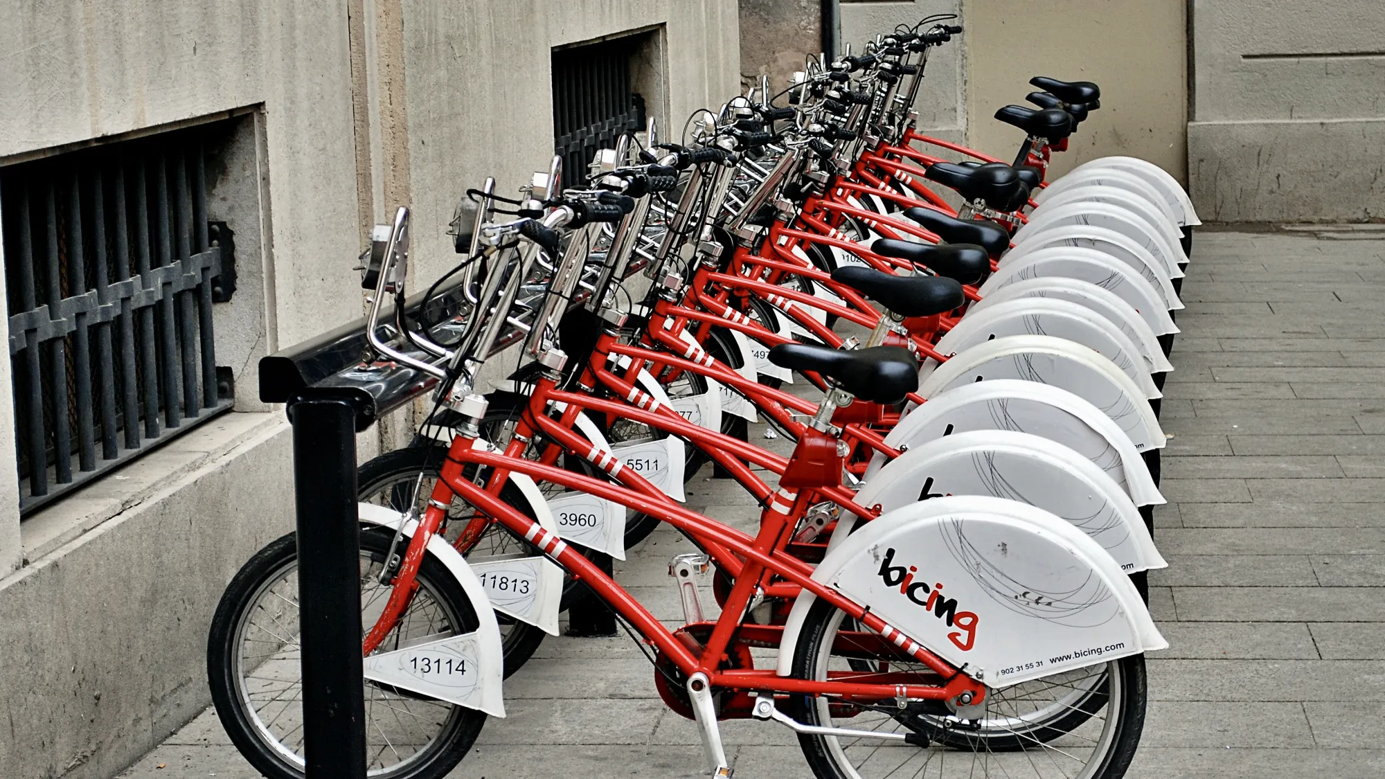 A bike rack full of rental bicycles in Barcelona. The bikes are red and have a white faring on the back wheel