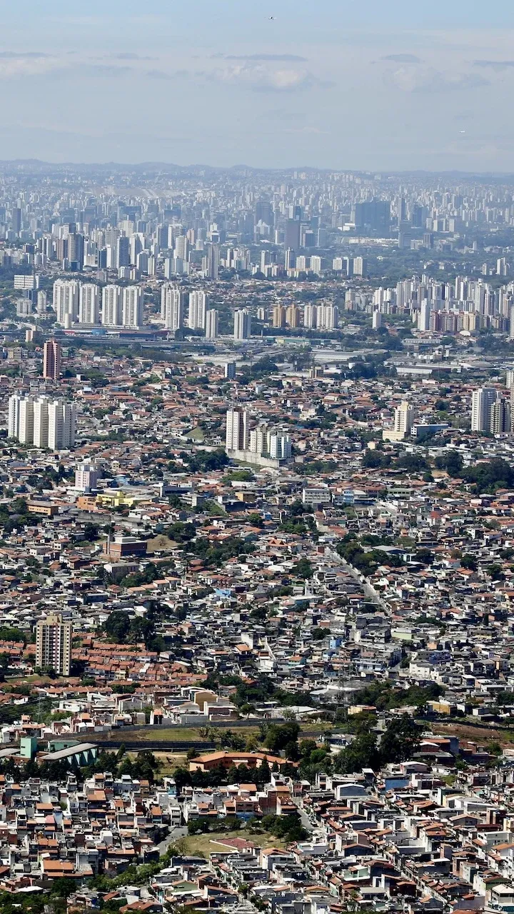 An aerial photo of São Paulo. Buildings stretch as far as the eye can see. In the foreground the buildings are low lying, but further into the distance there is an abundance of tower buildings.
