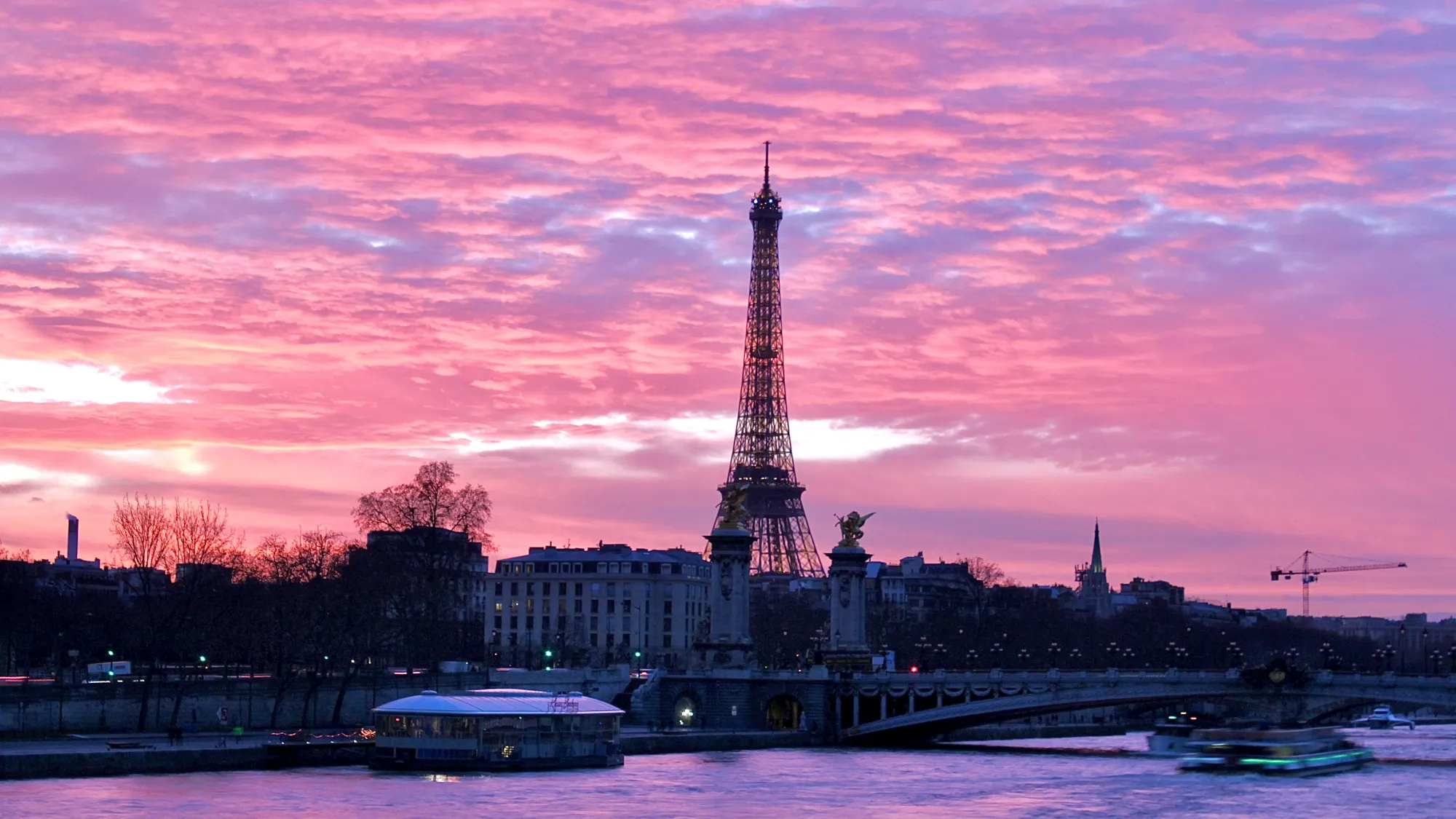 Paris' Eiffel Tower with a stunning pink sunset. The sunset makes the fluffy clouds pink and is reflected in the water of the river Seine in the foreground