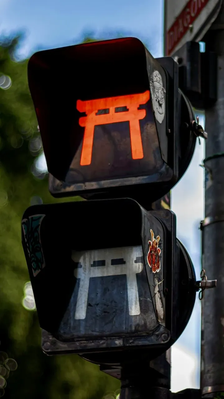 A traffic light in the Liberdade area of São Paulo. The Red light is illuminated, but instead of typical circular lights, the red light is in the shape of a traditional Japanese Tori gate.