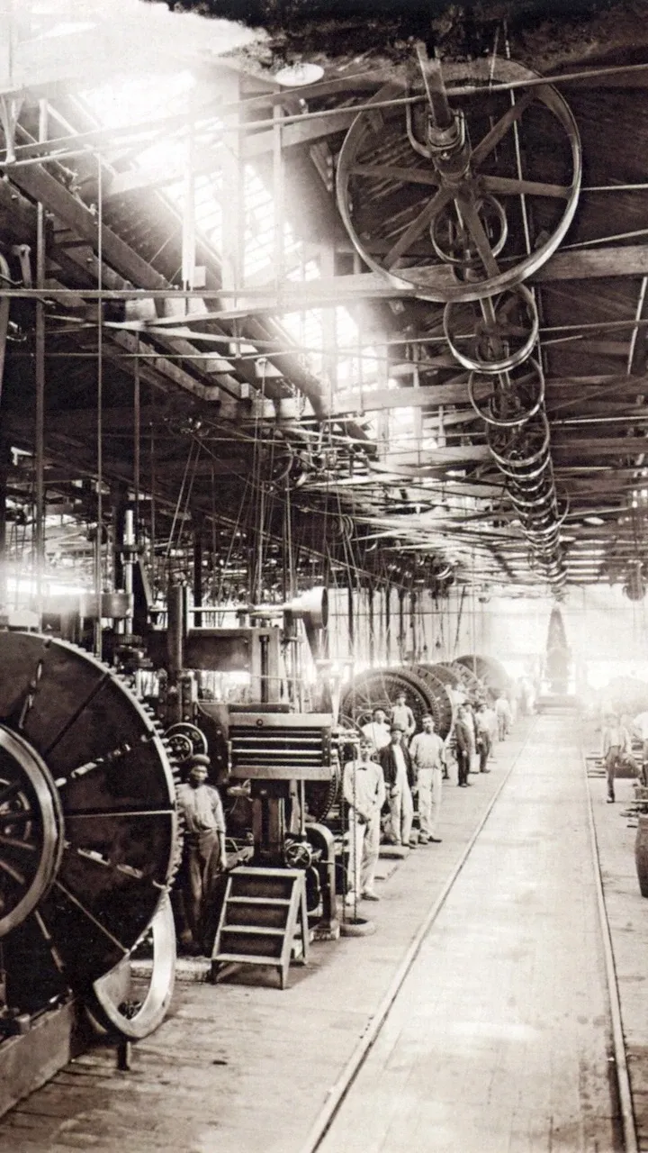 A black and white photograph from 1880. It shows the inside of an old factory in São Paulo. There are a few factory workers in shot.