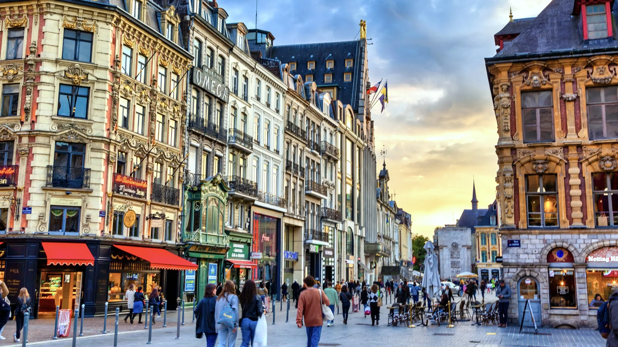 People enjoying their time shopping at an intersection of streets in Lille. Although the buildings are very traditional with ornate facades, the shops appear inviting and modern.