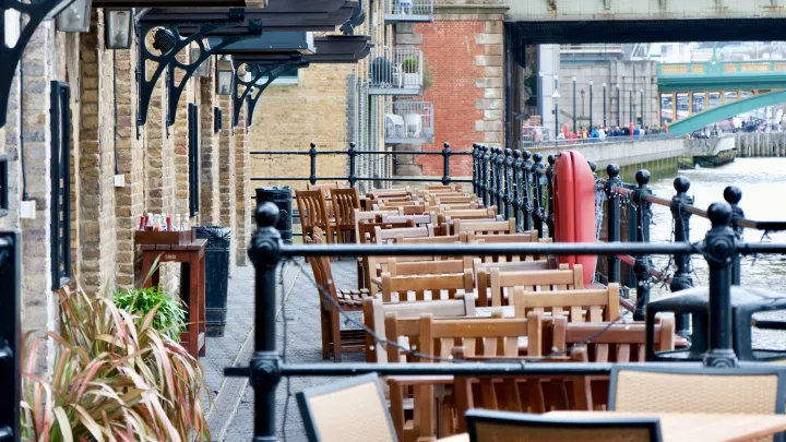 View of the an outdoors seating area at a London restaurant next to a canal, with two bridges going over the canal in shot.
