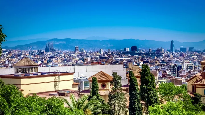 View over the sunlit Barcelona skyline, with La Sagrada Familia and the Glòries Tower poking out above the characteristically European flat cityscape. 