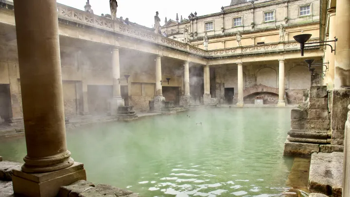 The Great Bath at the Roman Bath in Bath. Steam is emanating from the warm spring water, which has green hue.